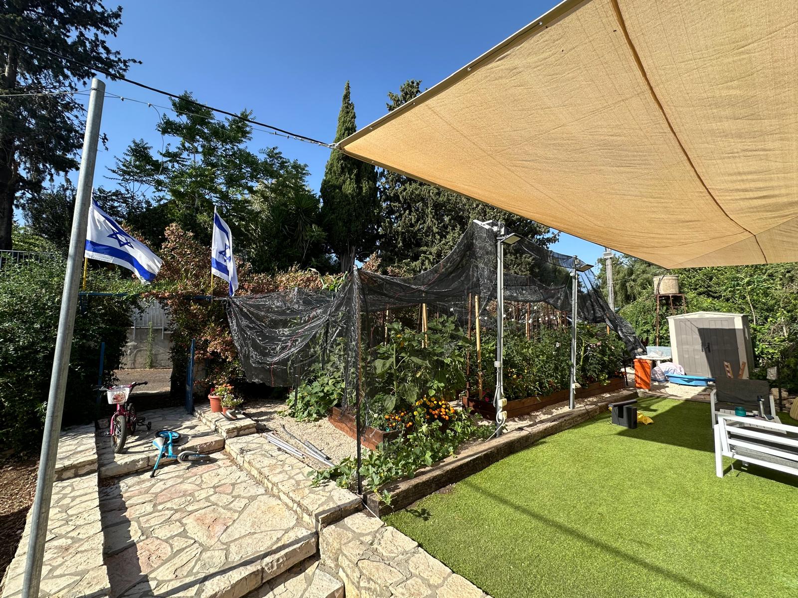 מבט רחב על הגינה הביתית: ערוגות, רשת צל ודגלים